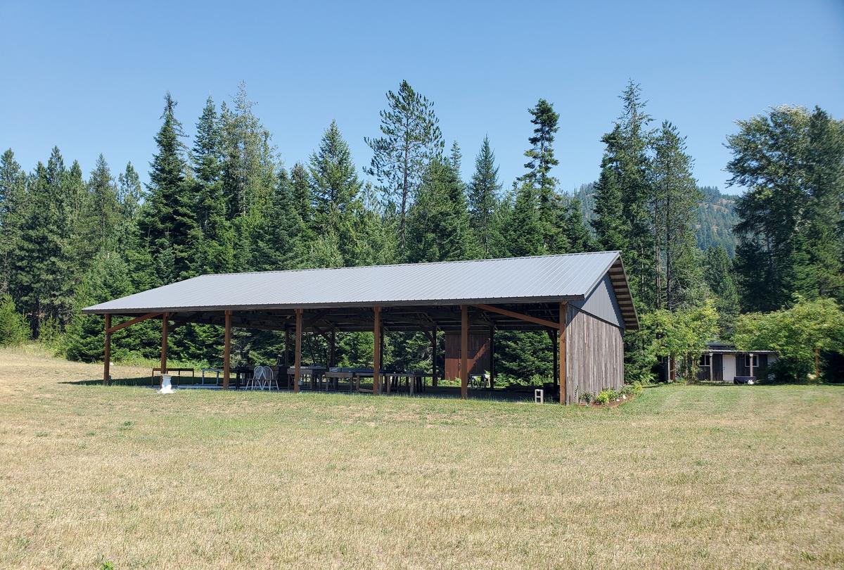 Side view of the open timber-frame pavilion standing in the golden meadow